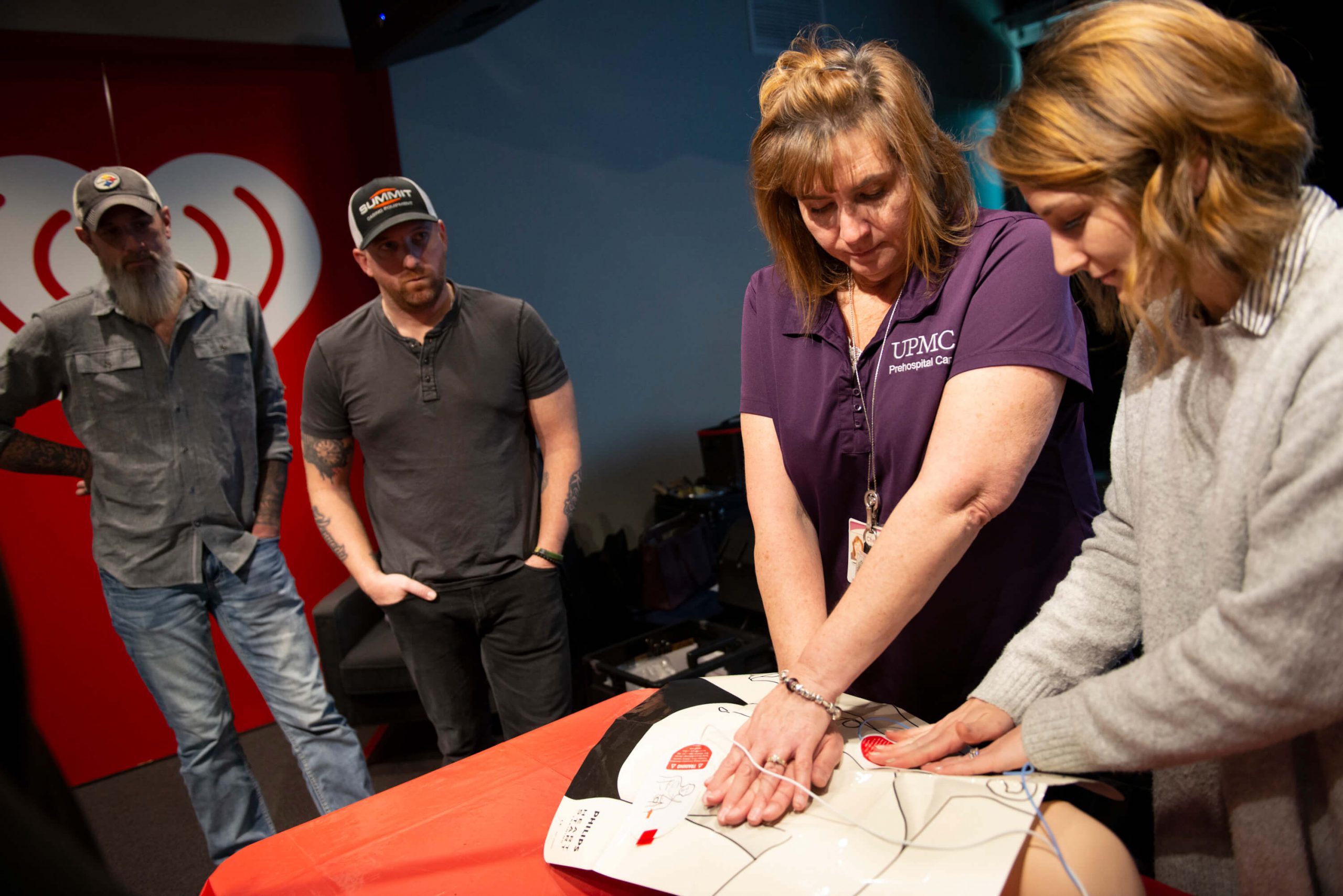 Woman teaching how to give CPR on a dummy at a iHeartRadio event.