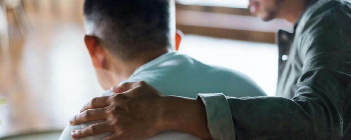 Man with a hand on the back of another man, comforting him