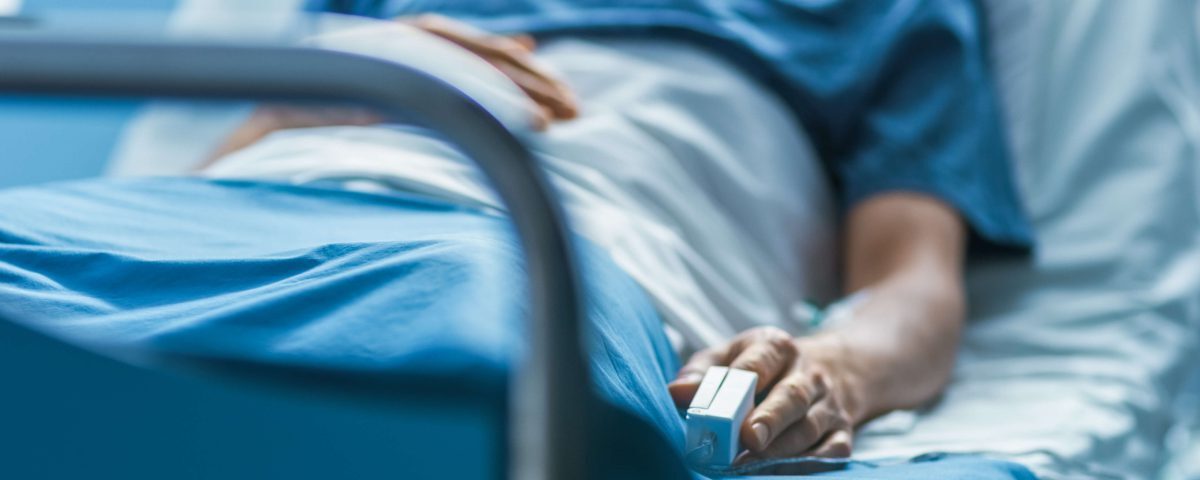 Person laying in a hospital bed with a heart rate monitor on his finger