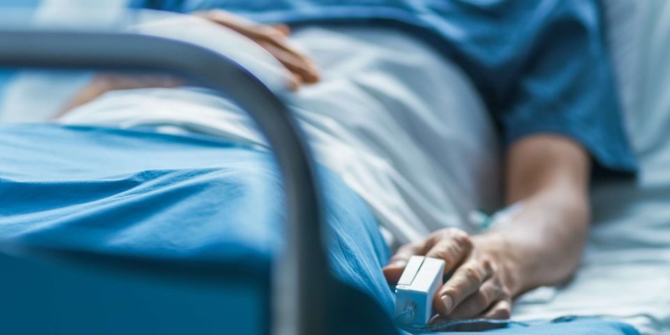 Person laying in a hospital bed with a heart rate monitor on his finger