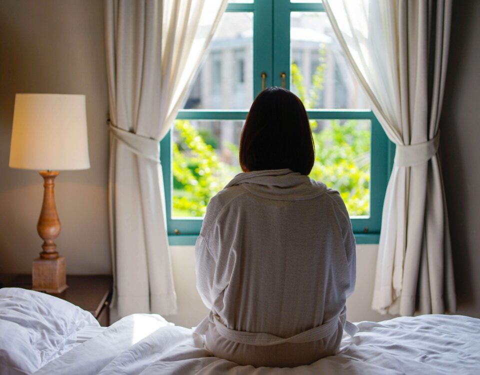 Woman with short dark hair sitting on a bed looking out a window